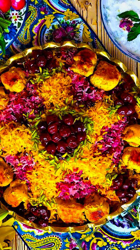 آلبالو پلو و مواد آلبالو پلو در یک سینی سنتی گرد به همراه مرغ و برنج زعفرانی و برنج قرمز و خلال پسته و آلبالو در وسط آن است
